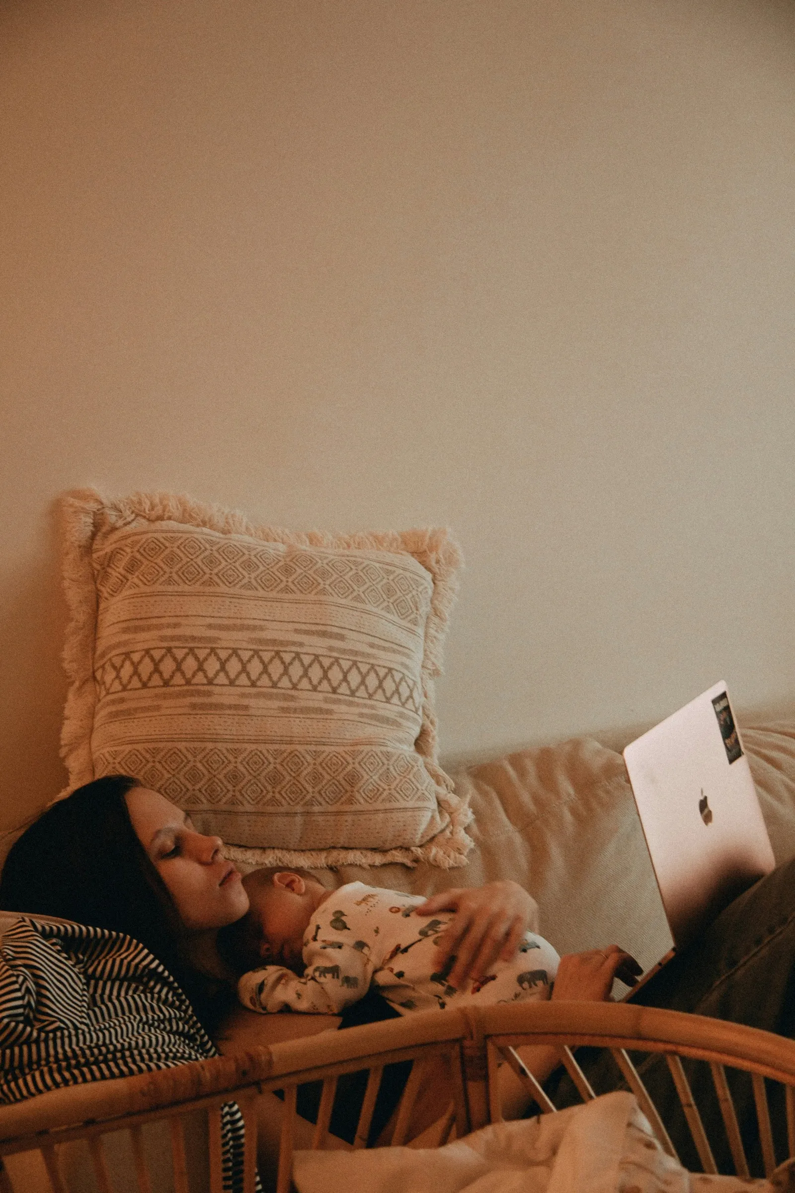 Retailer managing her online store on a laptop at home while a baby sleeps on her chest