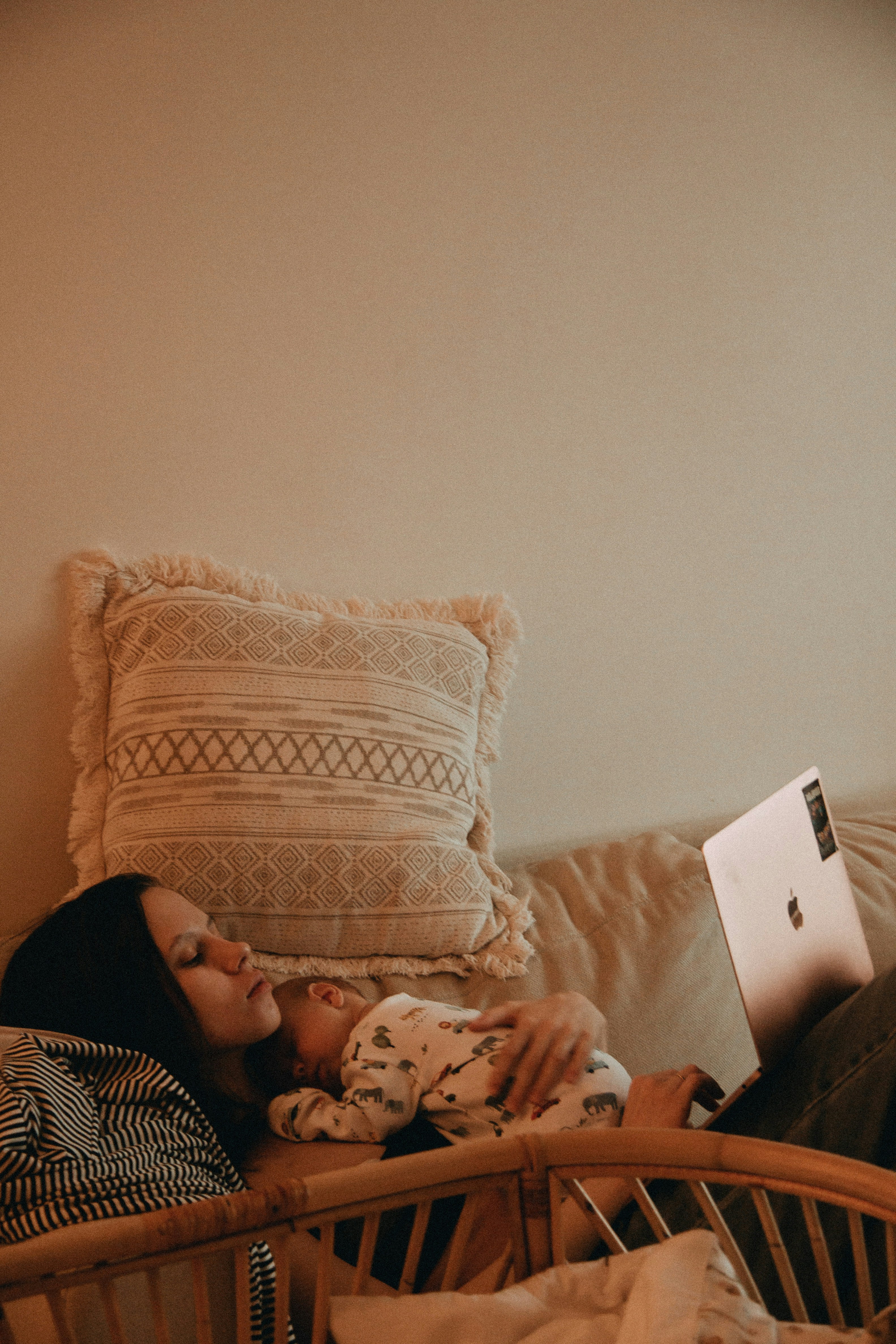 Retailer working on a laptop at home while a baby sleeps on her chest